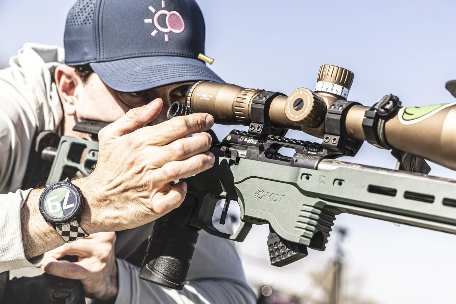 A precision rifle shooter behind a bolt-action rifle in a chassis, with a Garmin watch on his left wrist showing 79 seconds remaining on a running stage.